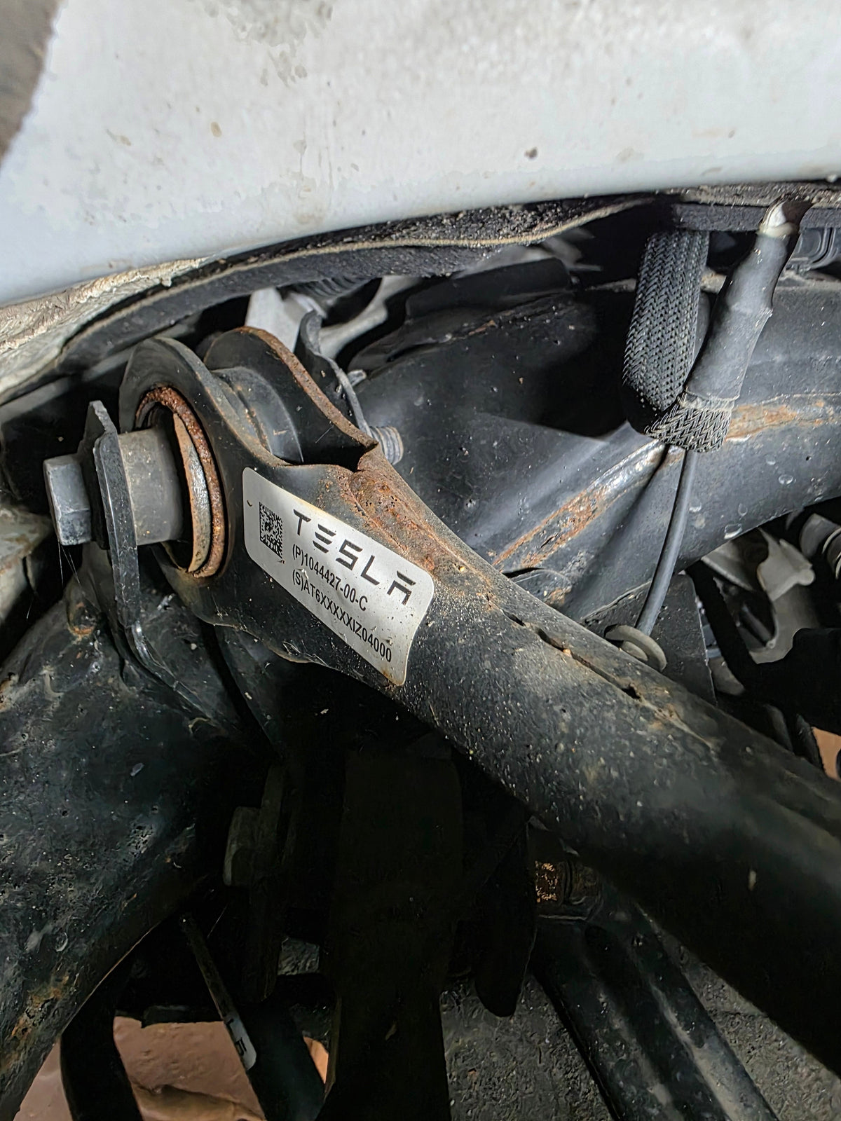 Rostiger Querlenker mit Tesla-Teileetikett an der Hinterachse – Garantie-Endcheck Leipzig